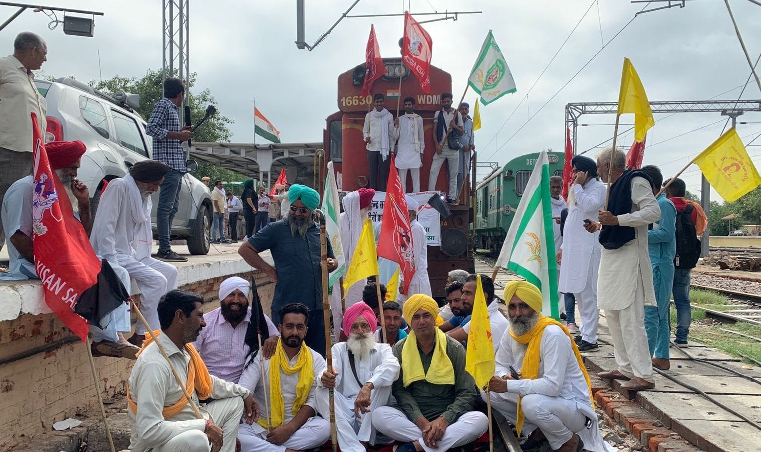 रेलवे स्टेशन पर रेलगाड़ी को रोककर पटरी पर बैठे किसान।