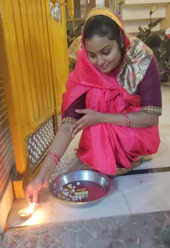 छोटी दिवाली पर घर के दरवाजे पर दीया जलाती महिला।  संवाद