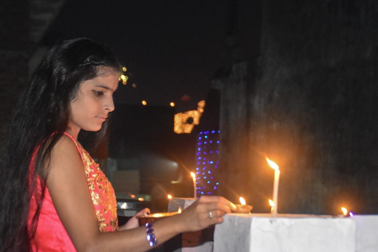 दीये जलाकर घर को रोशन करती युवती ।