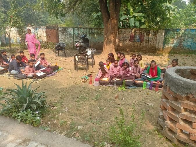 फोटो-08एयूआरपी-22- स्कूल के मैदान में जमीन पर बैठ कर पढ़ाई करते छात्र-छात्राएं। संवाद