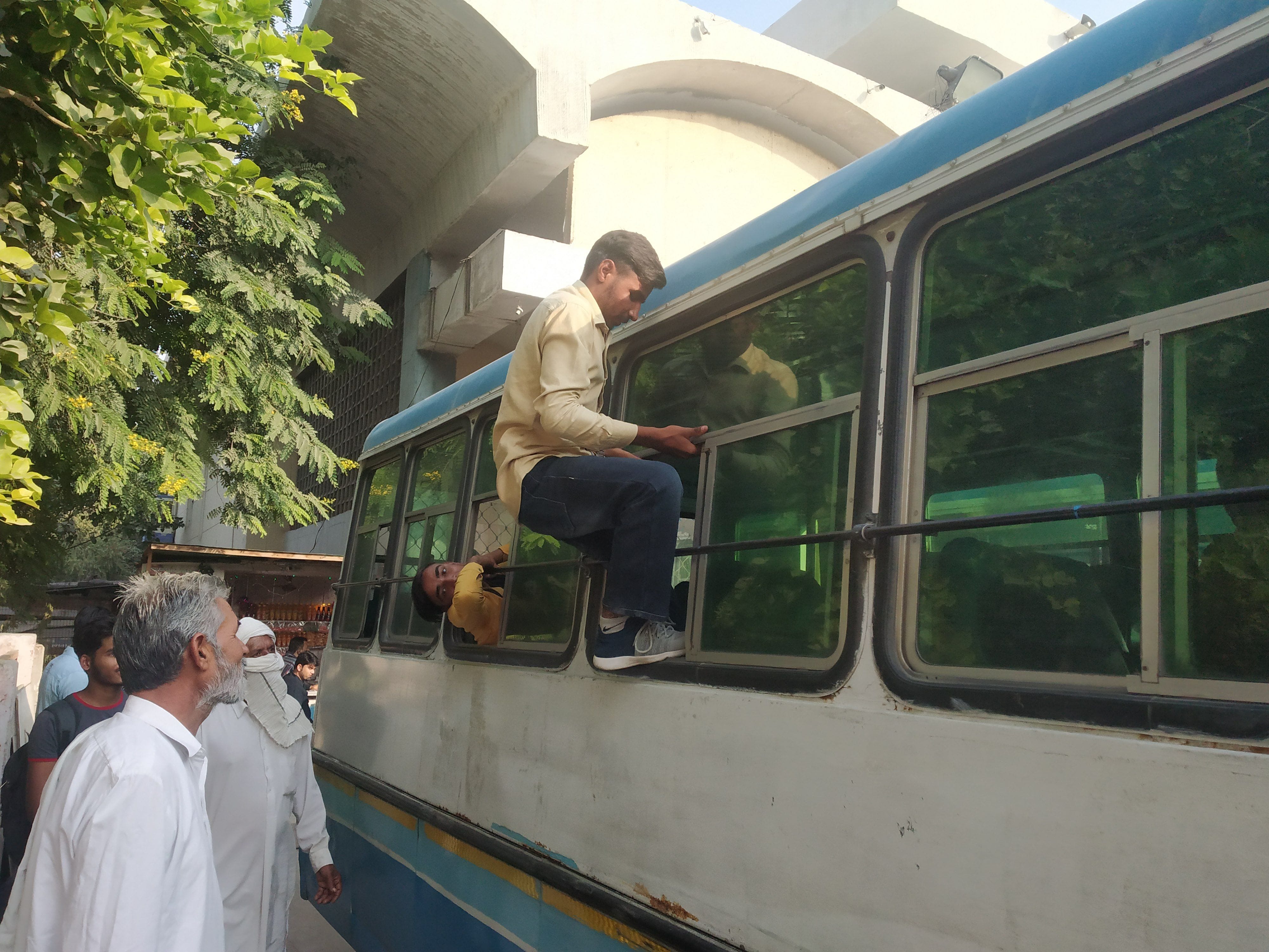 बस में चढ़ने की जगह न मिलने के कारण खिड़की से बस में प्रवेश करता छात्र। 