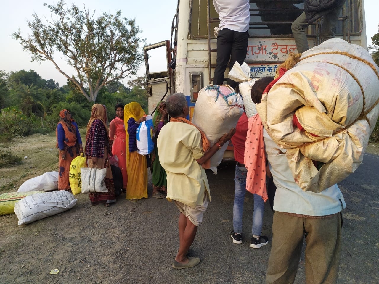 बस पर अपना अपना सामान रखते आदिवासी लोग बस पर अपना अपना सामान रखते आदिवासी लोग