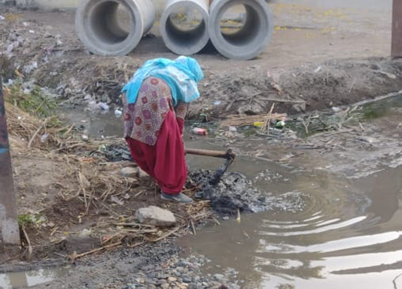 खटौली में सड़क पर भरे पानी का निकालने के लिए नालियों की सफाई करती महिला खटौली में सड़क पर भरे पानी का निकालने के लिए नालियों की सफाई करती महिला
