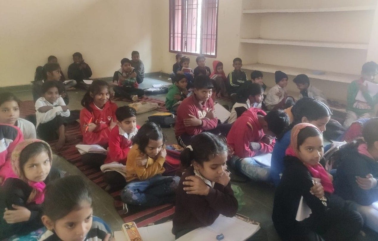  ठिठुरती ठंड में बिना डेस्क जमीन पर बैठ पढ़ाई करते सरकारी स्कूल के बच्चे। संवाद
