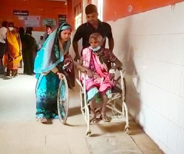 मेडिकल कालेज में टूटे व्हील चेयर का पहिया हाथ में लेकर वृद्ध मां को सम्हालते तीमारदार। संवाद