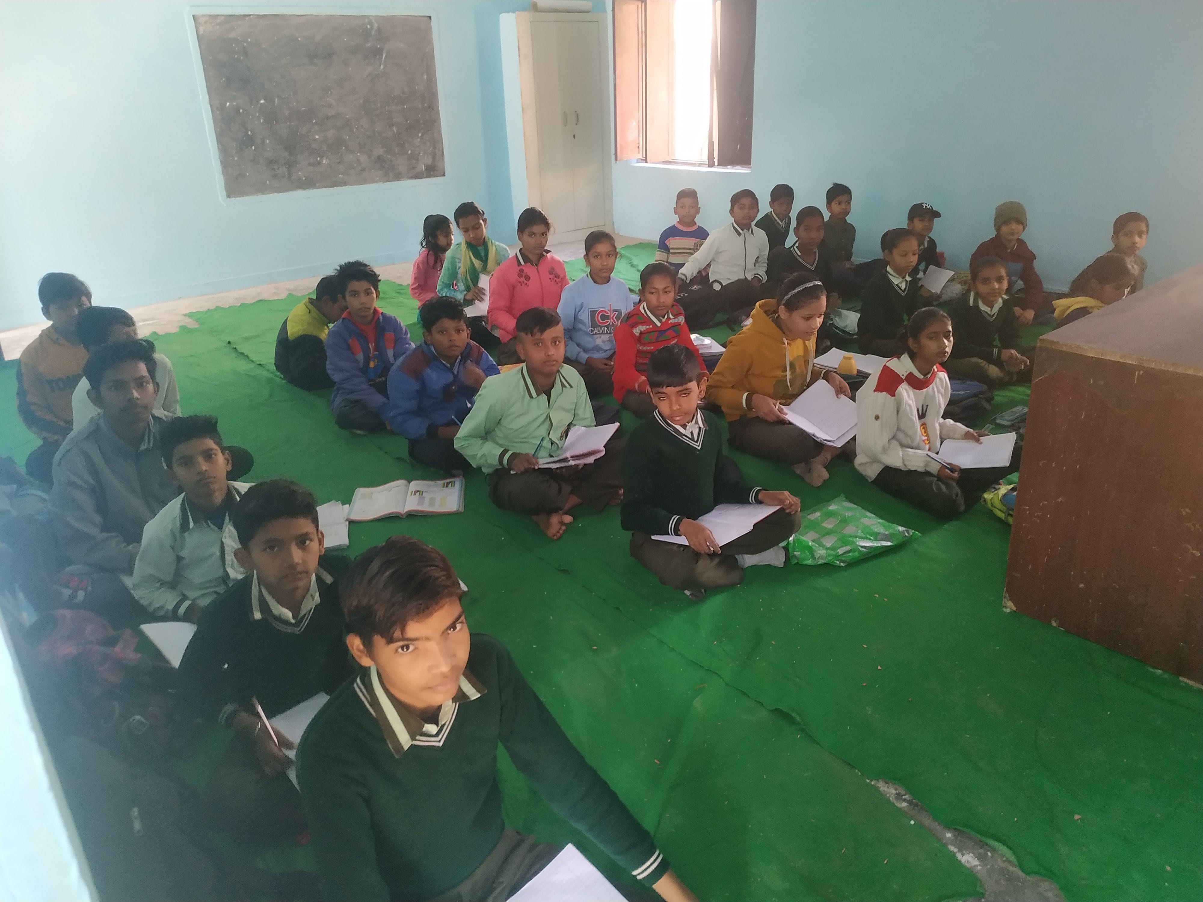 डेस्क के अभाव में दरी पर बैठै विद्यार्थी। डेस्क के अभाव में दरी पर बैठै विद्यार्थी।