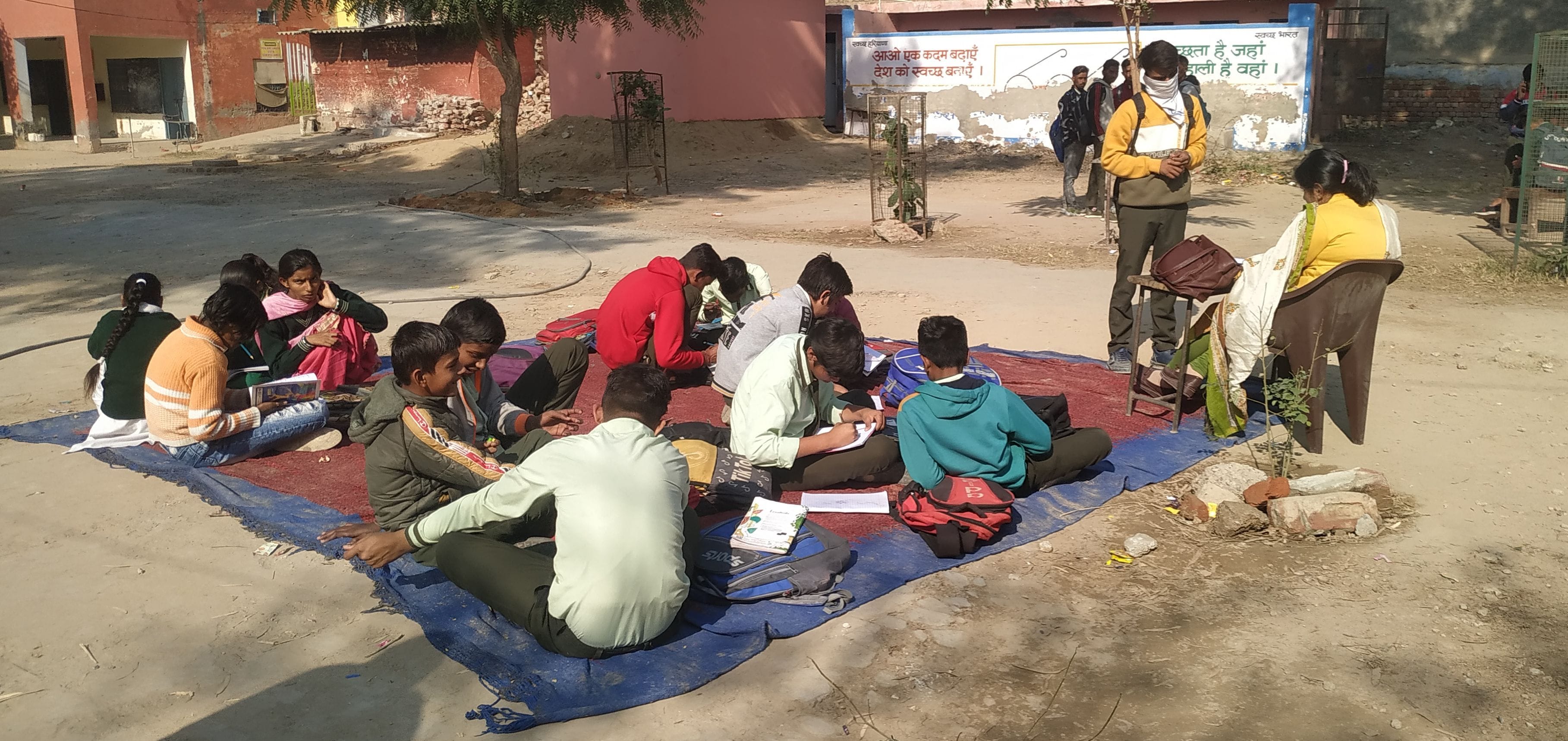 कमरों के अभाव में खुले में बैठे पढ़ाई करते विद्यार्थी। कमरों के अभाव में खुले में बैठे पढ़ाई करते विद्यार्थी।