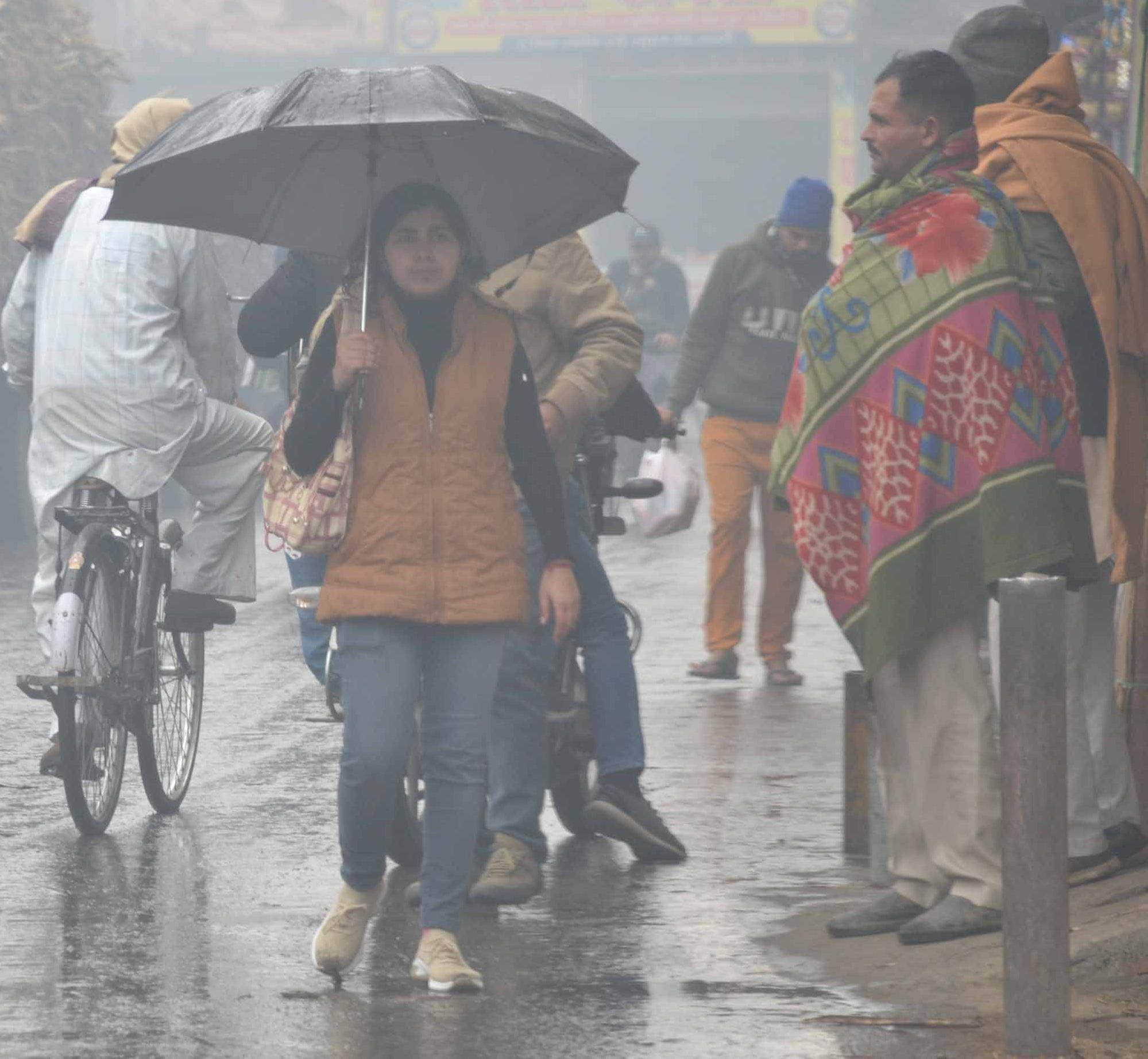 शामली हल्की बरसात में छाता लगाकर गुजरती महिला।