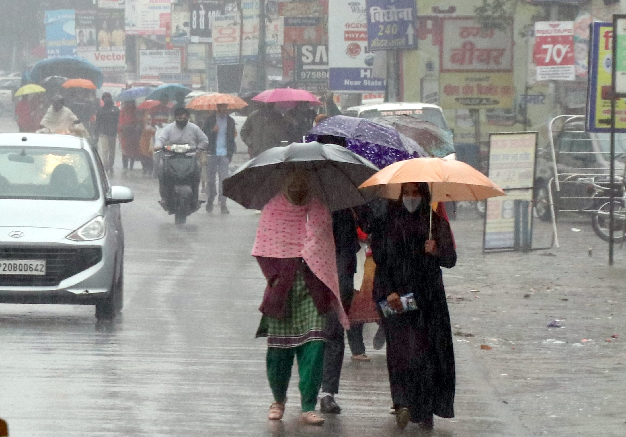 बिजनौर में बारिश में छाता लगाकर जाते लोग।