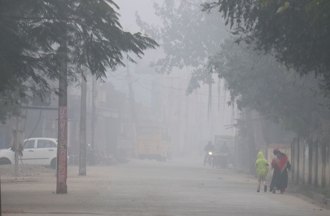 काशीपुर में कोहरे के दौरान एक मोहल्ले से गुजरते लोग