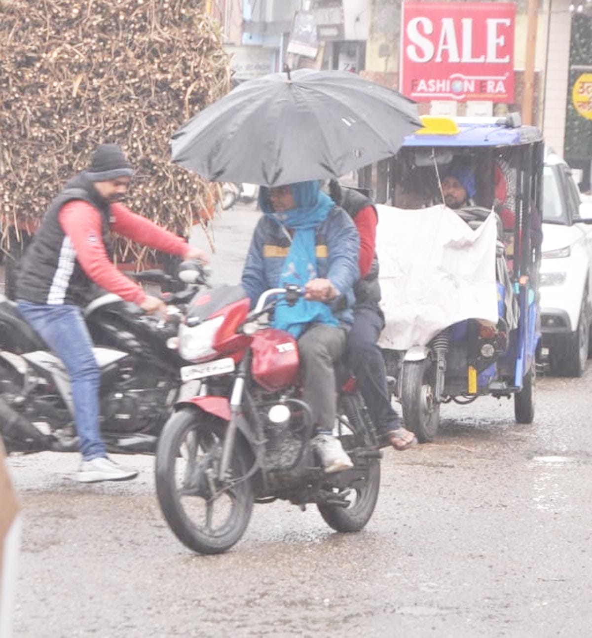 बारिश में बाइक पर छतरी लगाकर जाते युवक।
