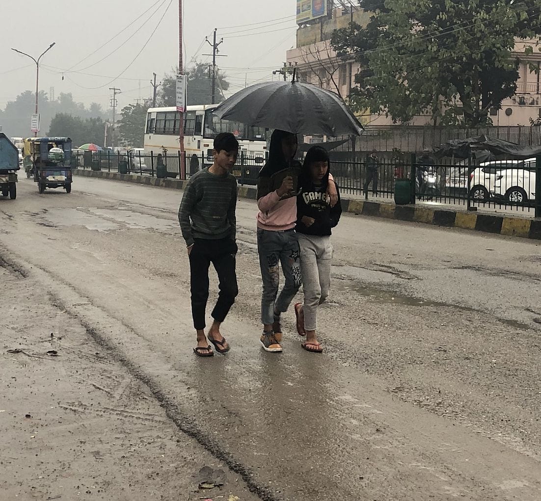 रुद्रपुर के नैनीताल हाईवे पर बारिश से बचने के लिए छाता लेकर गुजरते तीन दोस्त।