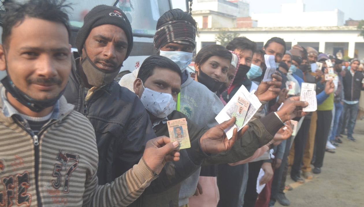 सरकारी स्कूल में मतदान करने के लिए अपना पहचान पत्र दिखाते लाइन में लगे युवक