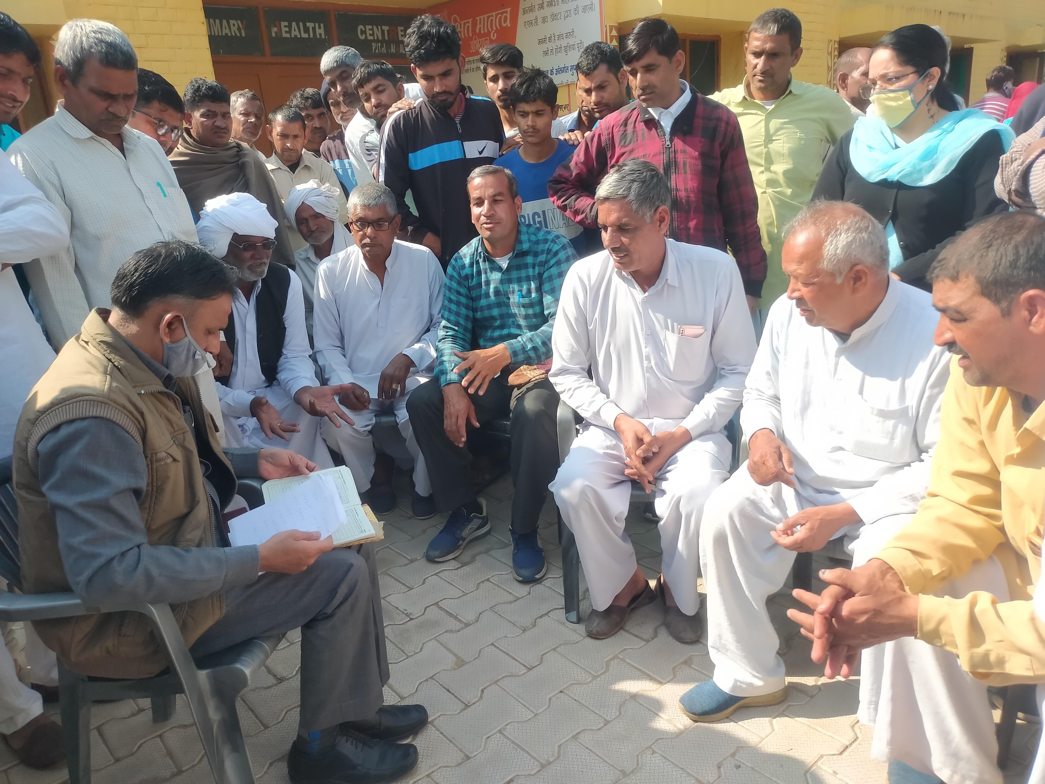 हांसी: ग्रामीणों के बीच बैठ कर हाजरी रजिस्टर चेक करते नायब तहसीलदार जगबीर सिंह।