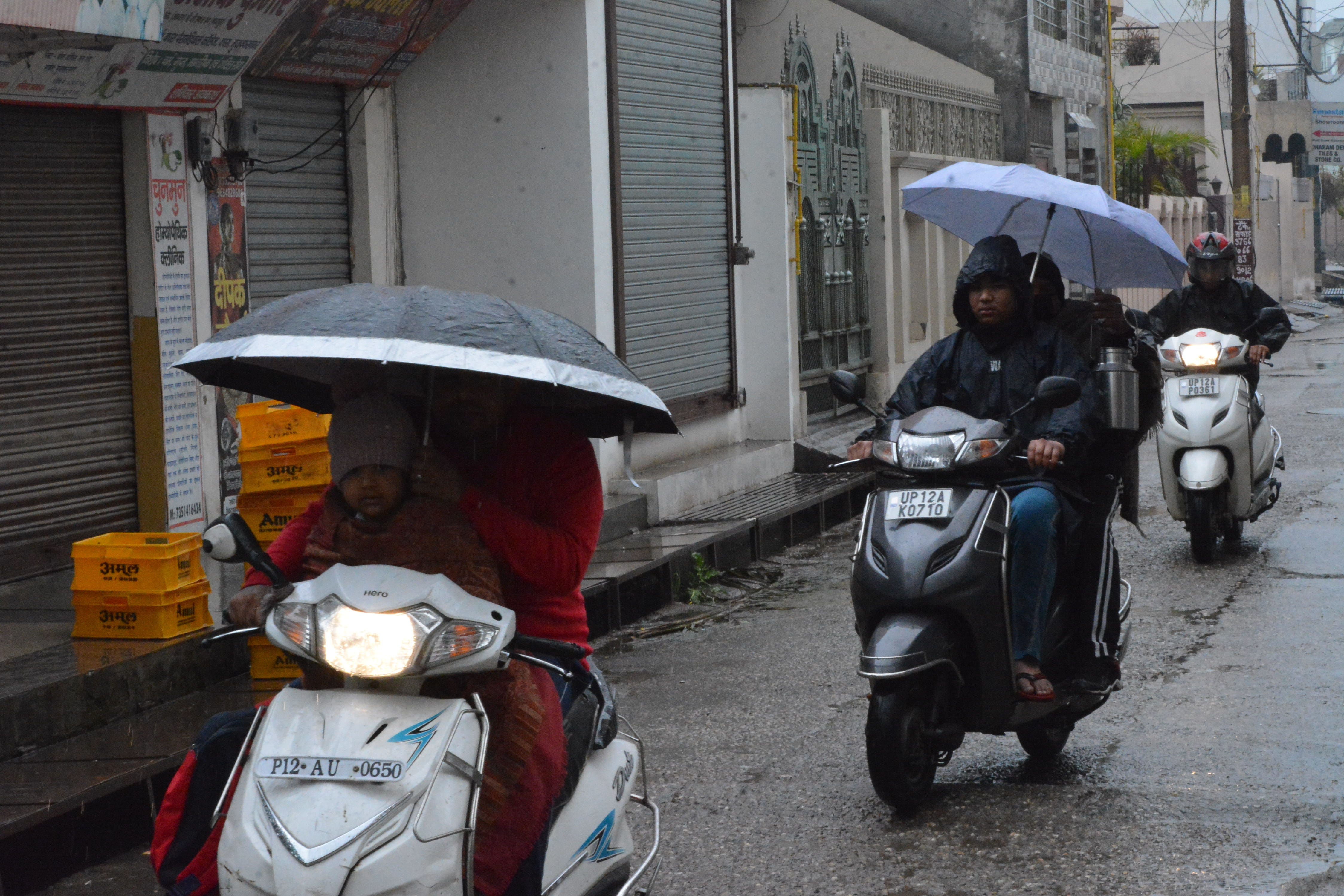 मुजफ्फरनगर में सुबह बारिश में छाता लेकर गंतव्य को जाते वाहन सवार। ।
