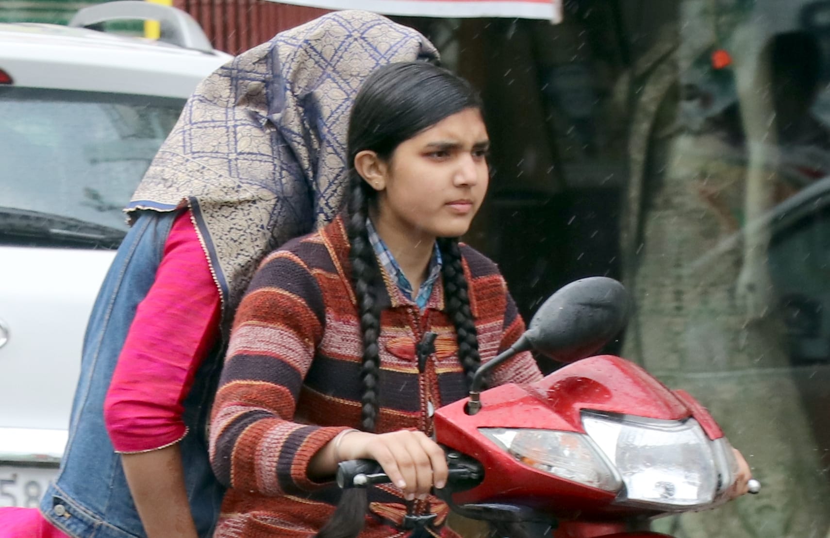 बिजनौर में बारिश में भीगती स्कूटी सवार युवती।