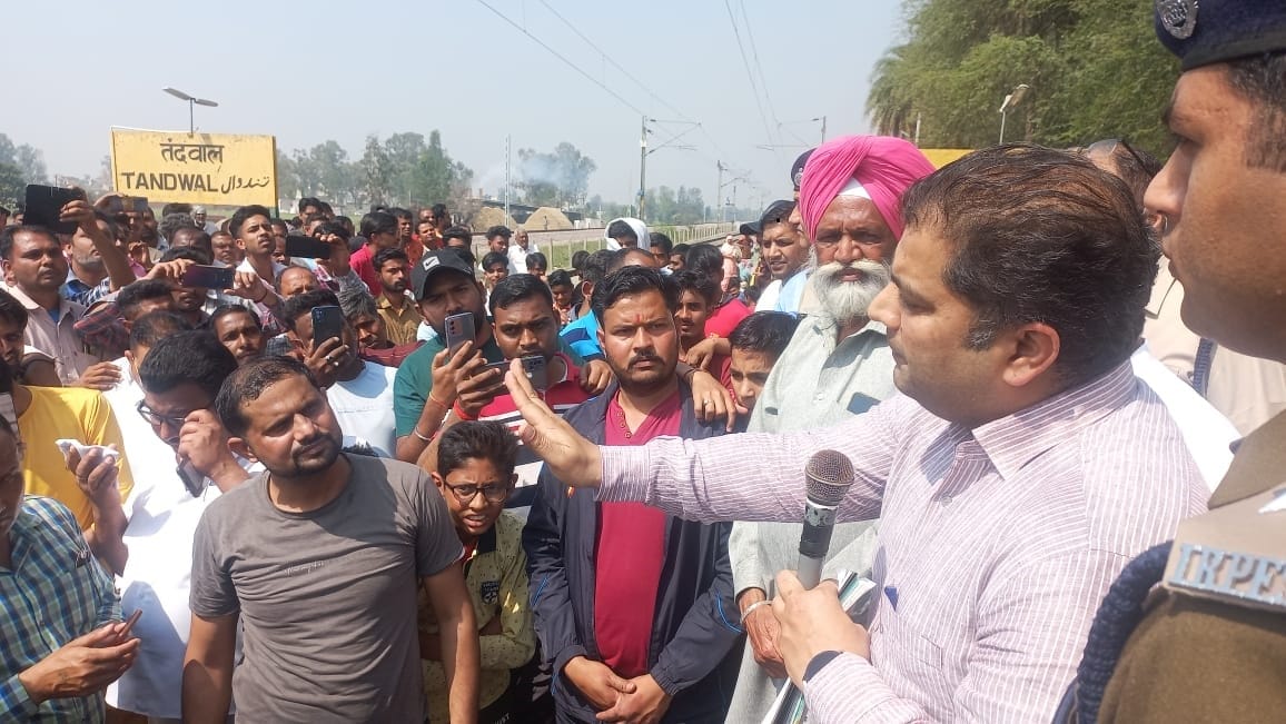 तंदवाल रेलवे स्टेशन  स्थित रेल ट्रैक पर जाम लगाकर बैठे लोगों को समझाते रेलअधिकारी
