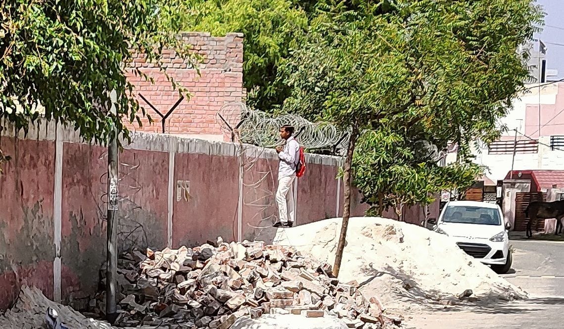  परीक्षा केंद्र के बाहर दीवार के ऊपर से अंदर की गतिविधियां देखता युवक। संवाद