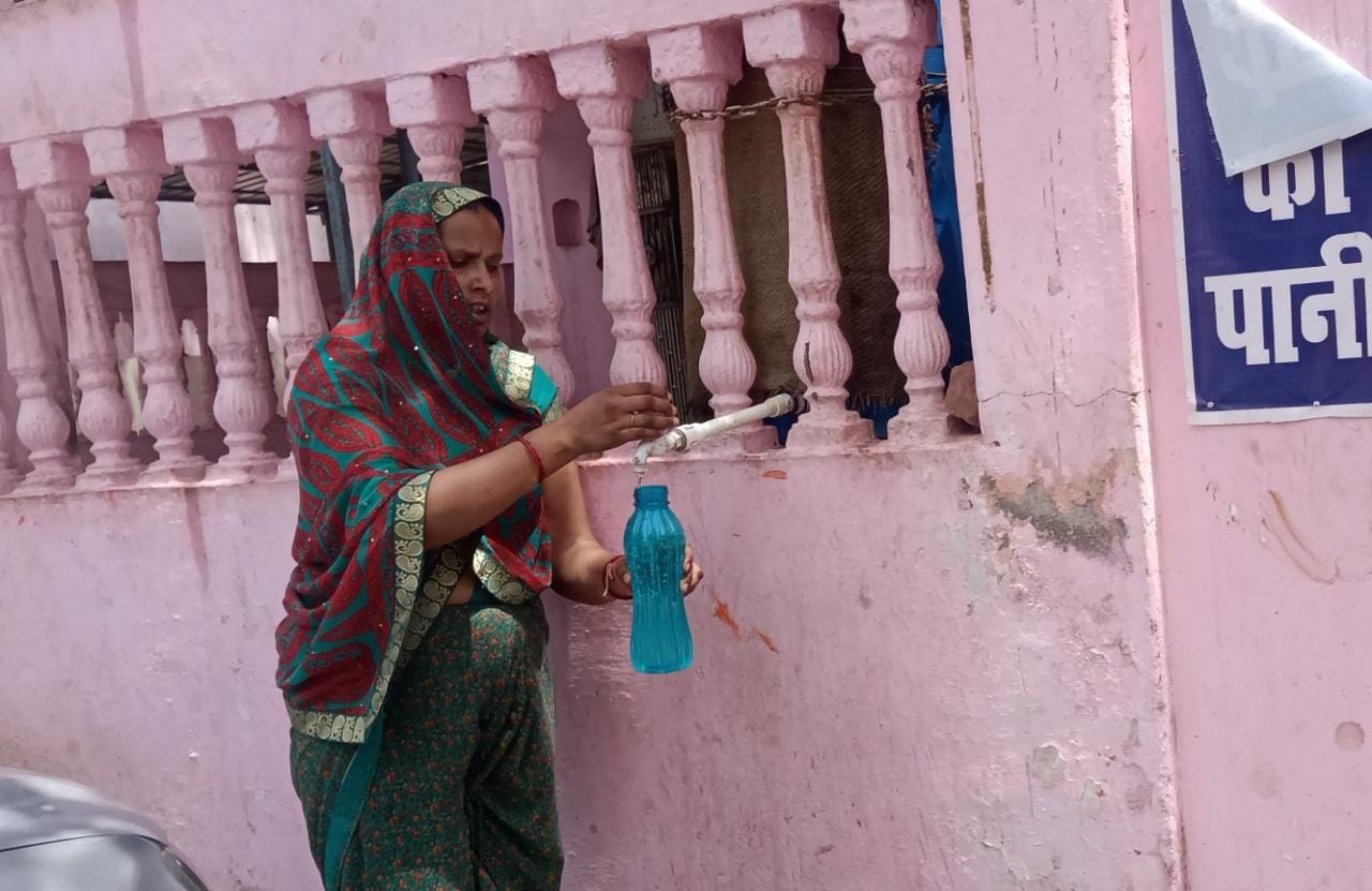 तहसील में मंदिर के पास लगी टोटी से बोतल भरती महिला
