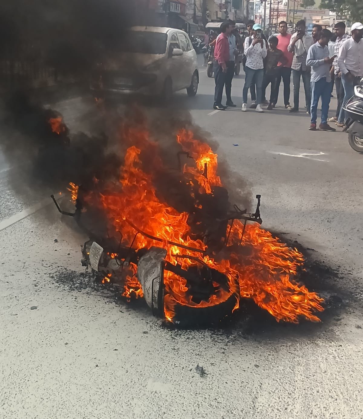   सुभाष चौक के पास धू-धू कर जलती स्कूटी को देखते लोग। संवाद