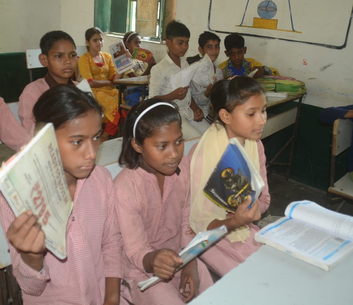 पूर्व माध्यमिक विद्यालय बली में गर्मी के कारण किताब से हवा करते छात्र-छात्राएं