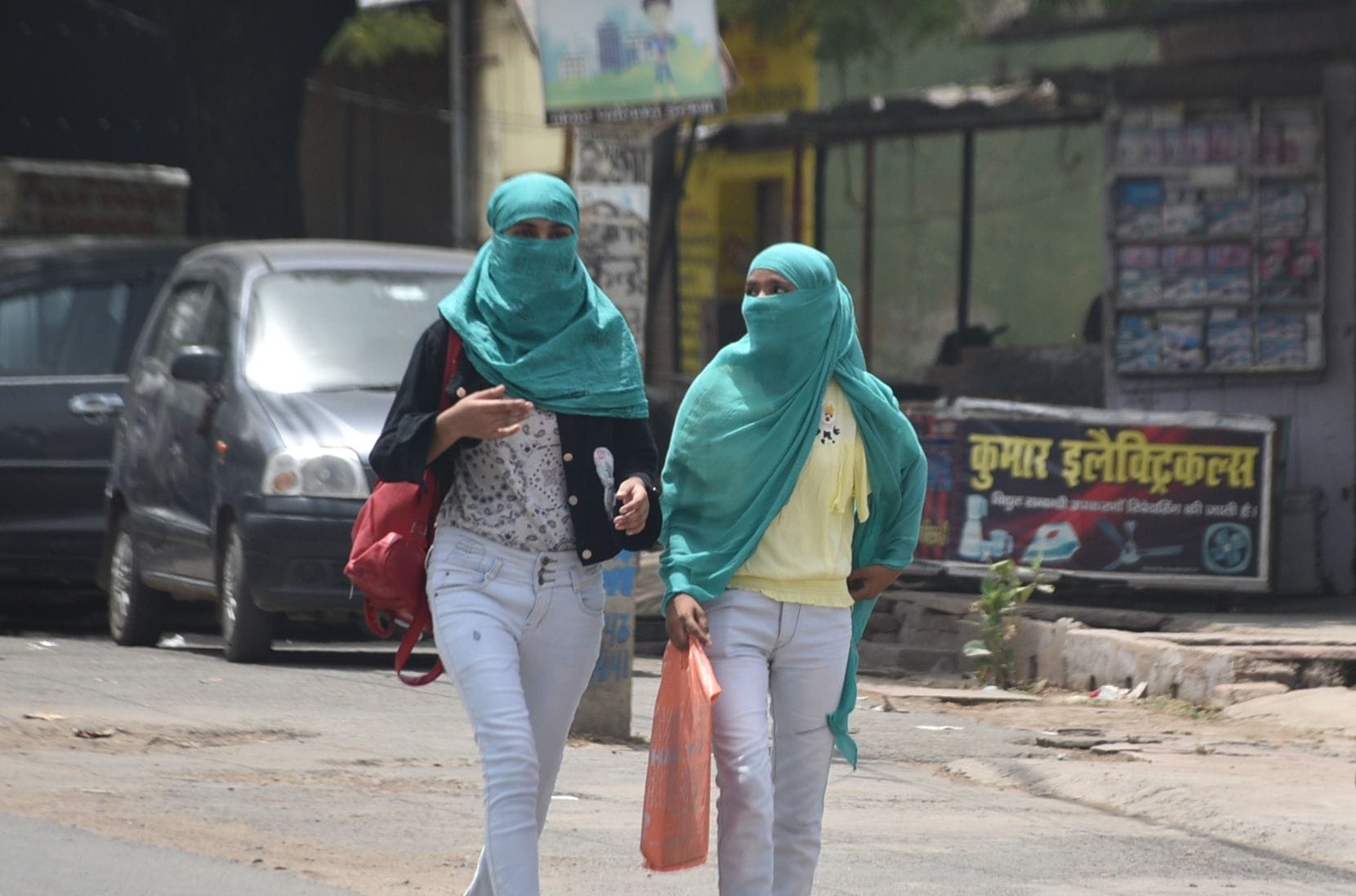 तेज धूप से बचने के लिए कपड़े से चेहरा ढंककर जातीं युवतियां। संवाद