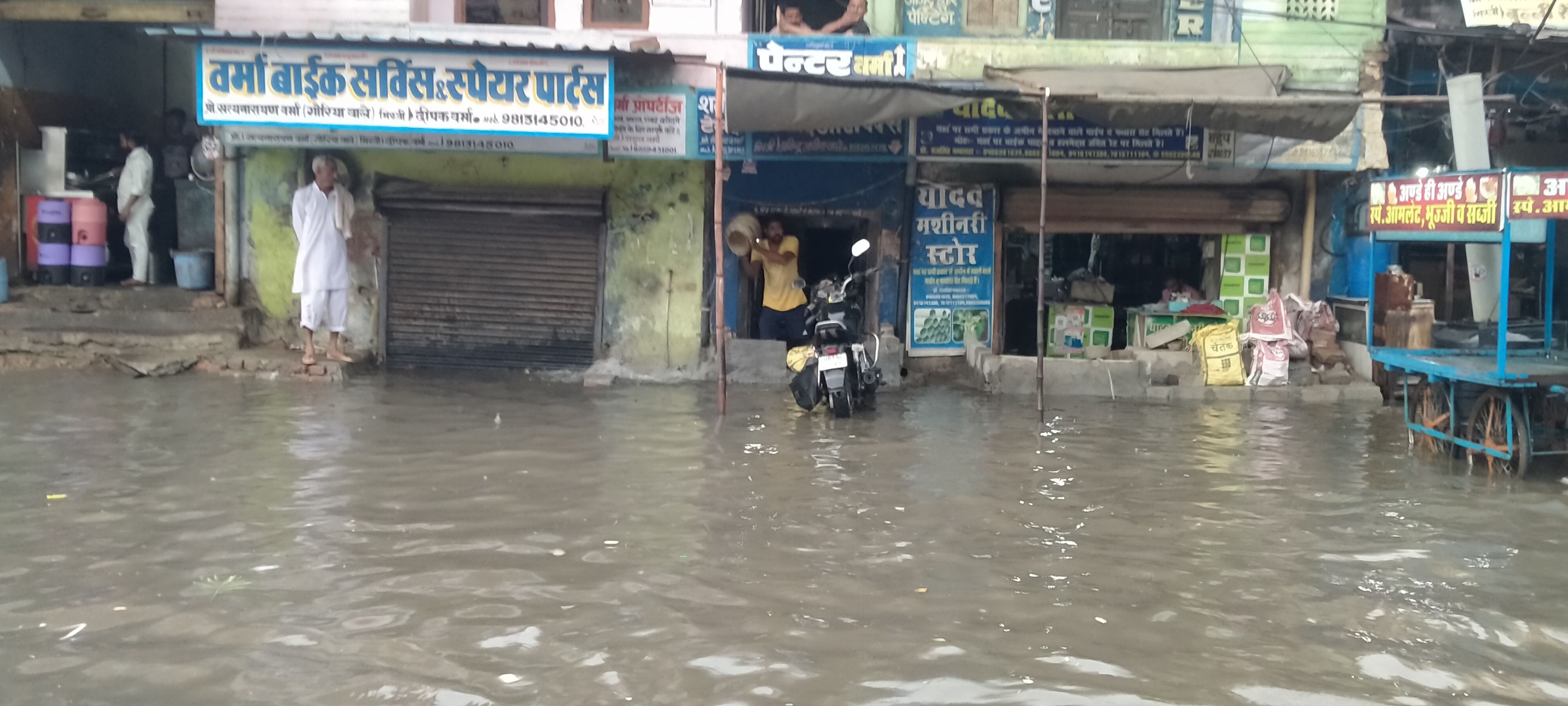 दुकान के अंदर घुसा पानी निकालता दुकानदार। दुकान के अंदर घुसा पानी निकालता दुकानदार।