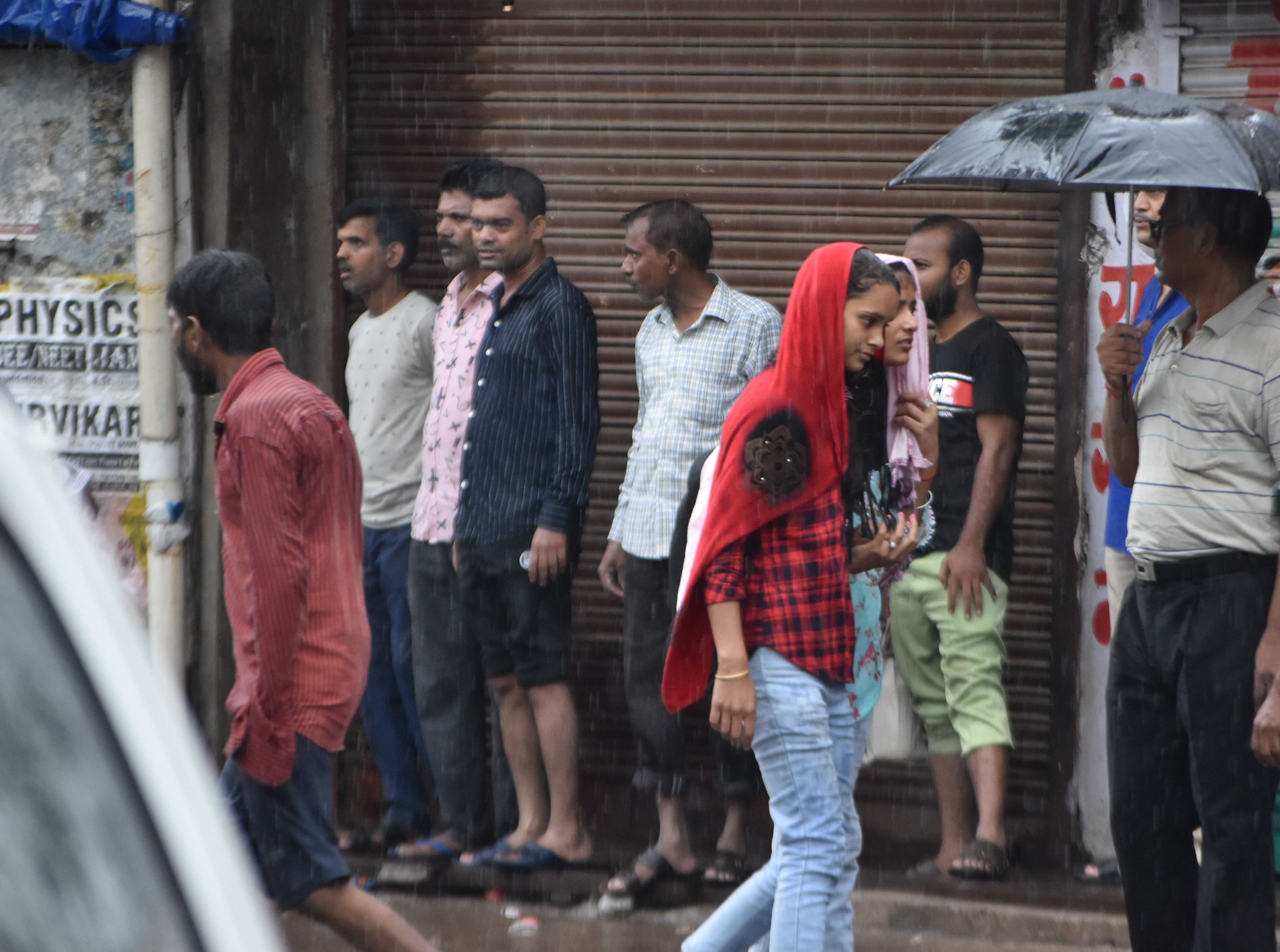 बारिश के दौरान बड़ा चौराहा पर वाहन का इंतजार करते लोग। संवाद