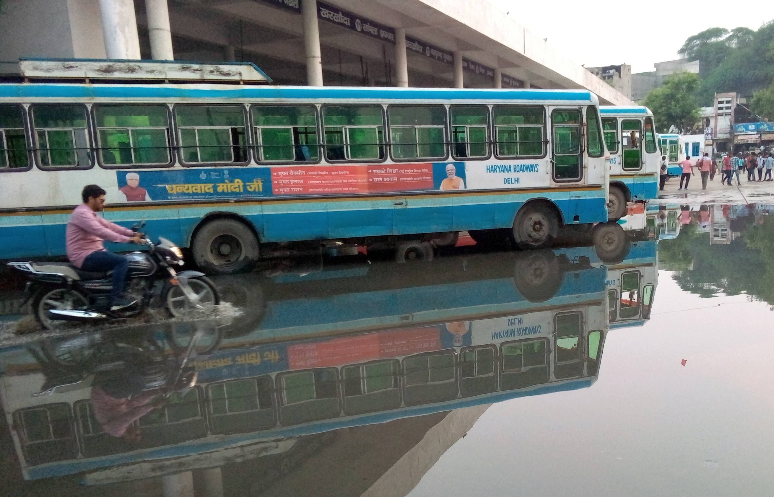  बस अड्डे में भरे पानी में खड़ी रोडवेज बस व गुजरता बाइक सवार। संवाद