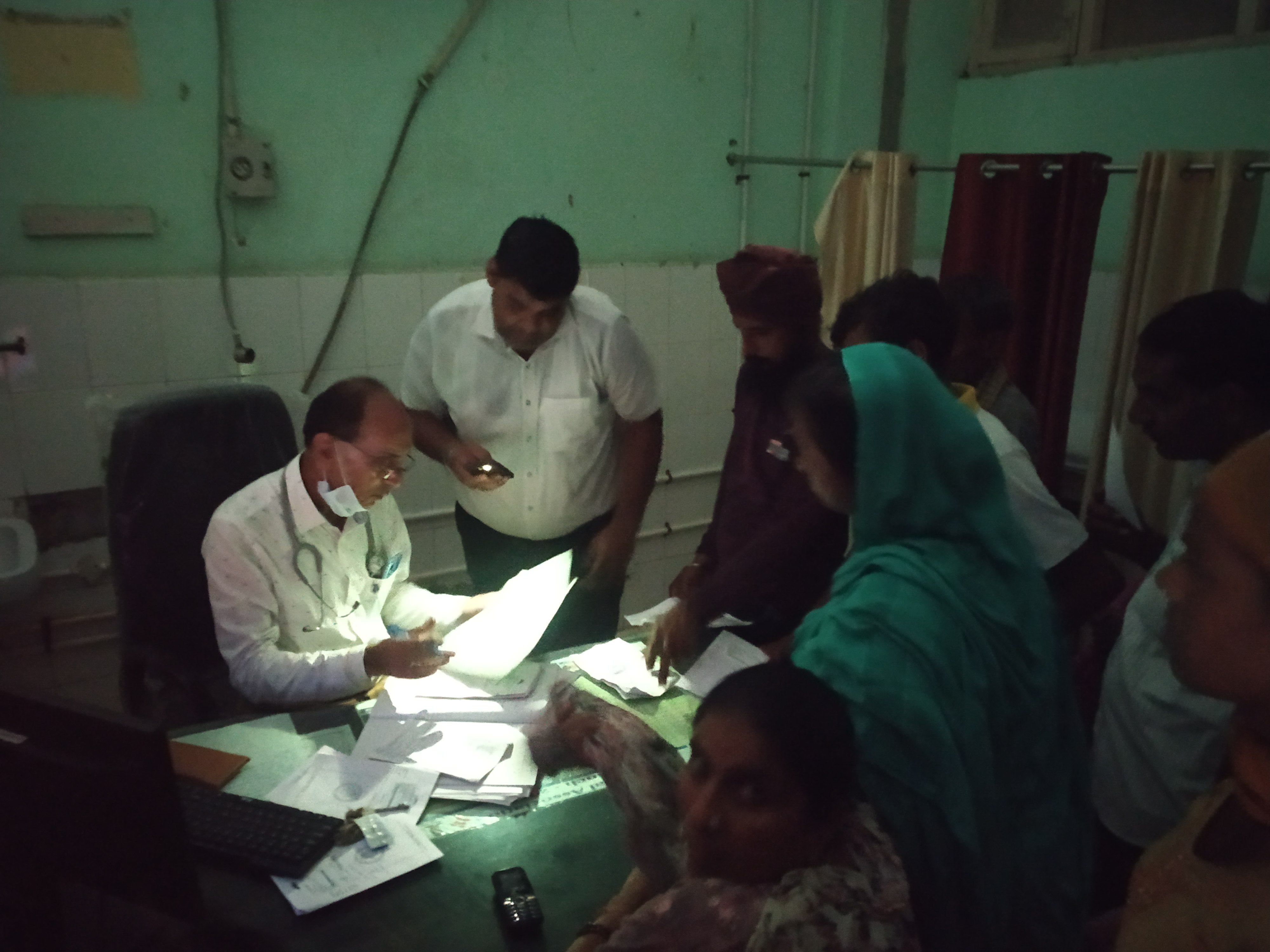मोबाइल की रोशनी में मरीज की पर्ची की जांच करते डॉक्टर। मोबाइल की रोशनी में मरीज की पर्ची की जांच करते डॉक्टर।