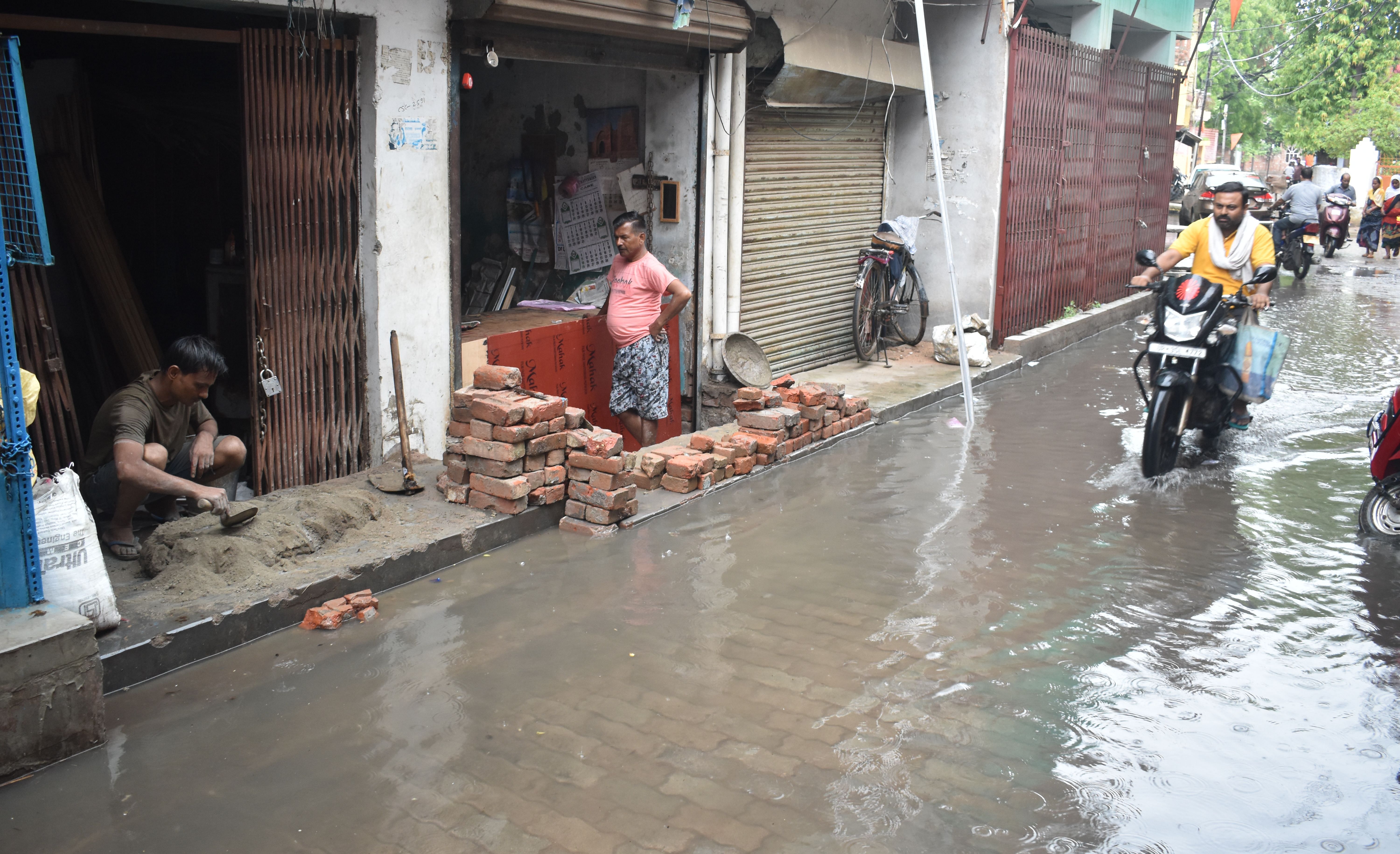 बारिश से हो रहे जलभराव के देखकर दुकान की फर्श ऊंची कराता दुकानदार। संवाद