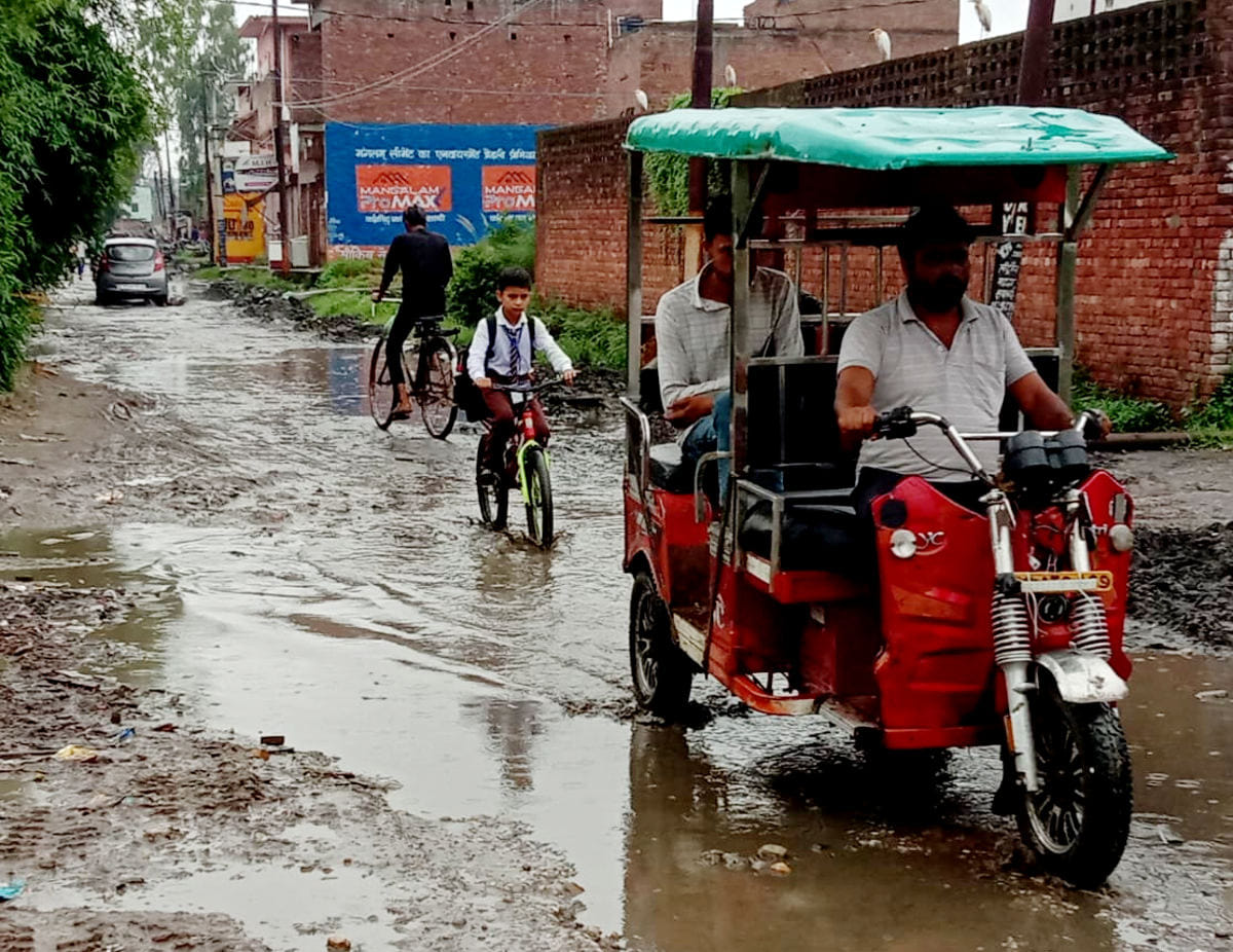 पुराना कलसिया रोड पर जलभराव के बीच से गुजरते वाहन और स्कूली बच्चा।
