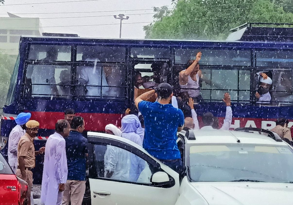 बारिश के दौरान गिरफ्तारी के बाद पुलिस बस में चढ़ते कांग्रेस कार्यकर्ता।