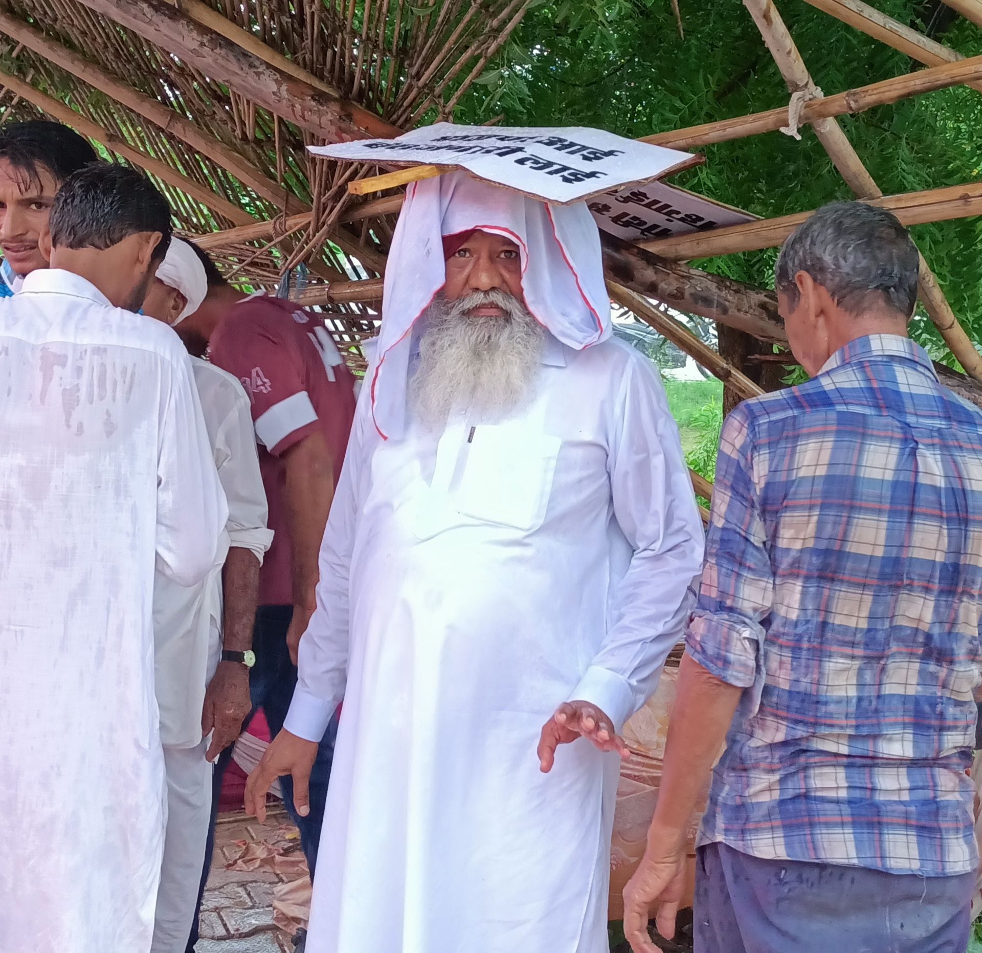 प्रदर्शन के दौरान अचानक बारिश आने के बाद बचाव को लेकर सिर पर तख्ती रखे हुए पूर्व विधायक चरणजीत सि?