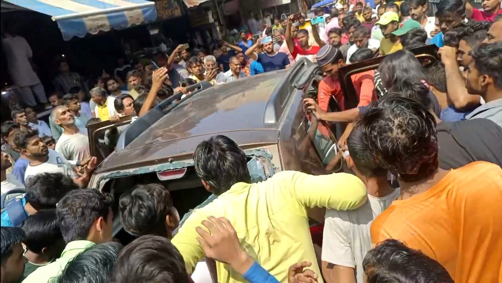 बागपत के शौकत मार्केट में कार में सवार युवकों को घेरे लोग। बागपत के शौकत मार्केट में कार में सवार युवकों को घेरे लोग।