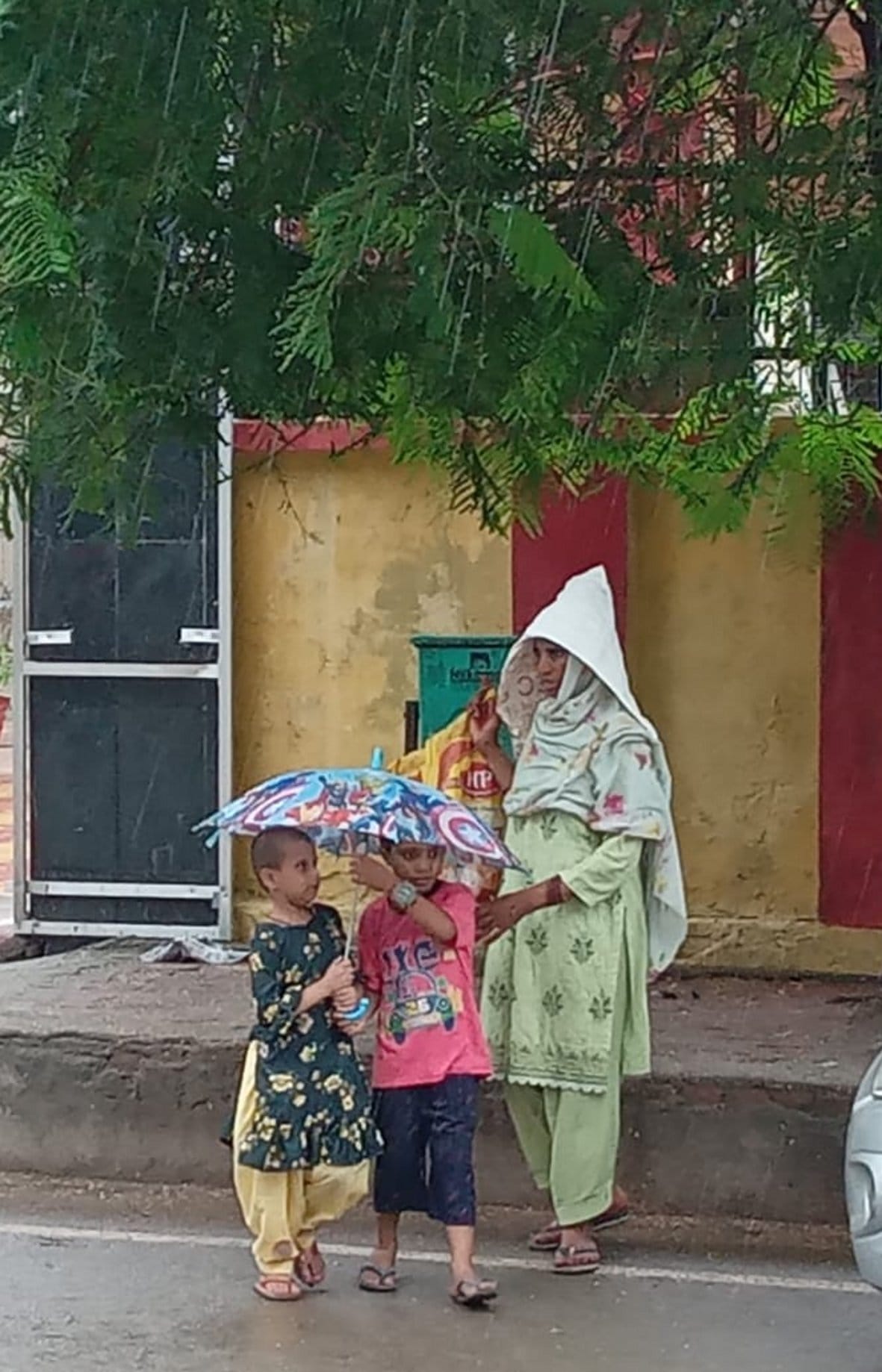 अरे बच्चों अभी यहीं रूक जाओं बारिश तेज हो रही है: बागपत में शुक्रवार को बारिश के दौरान पेड़ के नीचे