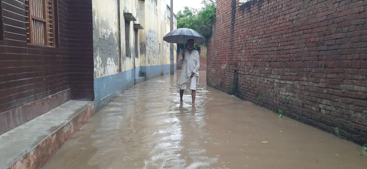 टीकरी गांव में भरे बारिश के पानी से गुजरता वृद्घ