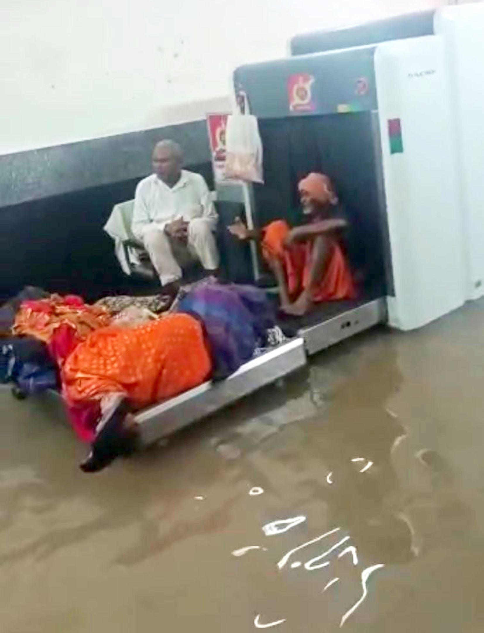 अयोध्या-रेलवेस्टेशन में जलभराव के कारण बैग स्कैनिग मशीन पर बैठे लोग।-संवाद अयोध्या-रेलवेस्टेशन में जलभराव के कारण बैग स्कैनिग मशीन पर बैठे लोग।-संवाद