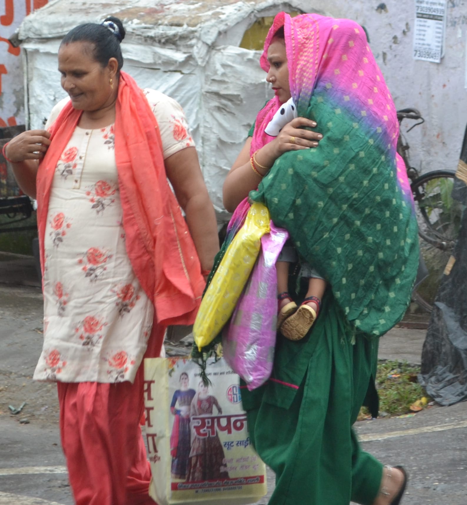 शामली बारिश में बच्चे को कपड़े से ढक ले जाती महिलाएं। शामली बारिश में बच्चे को कपड़े से ढक ले जाती महिलाएं।