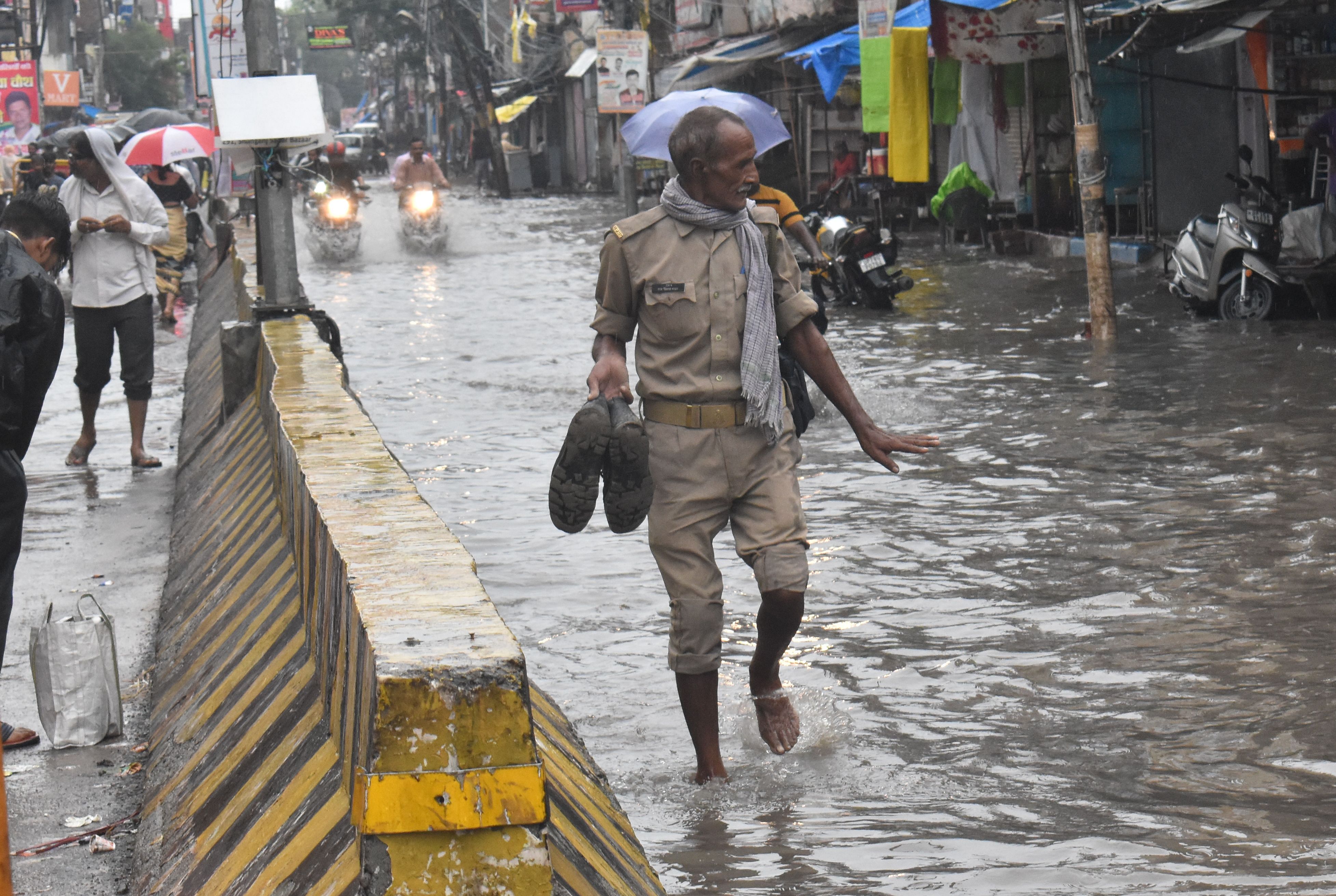 शाहगंज में सड़क पर हुए जलभराव के बीच जूते हाथ में लेकर जाता पुलिस कर्मी। संवाद