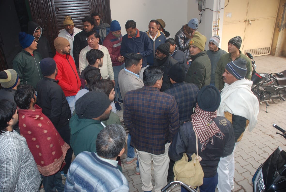 प्रधान लिपिक दीपक यादव का शव मिलने के बाद बागपत के गली नम्बर चार में घर के बाहर मौजूद पुलिसकर्मी व 