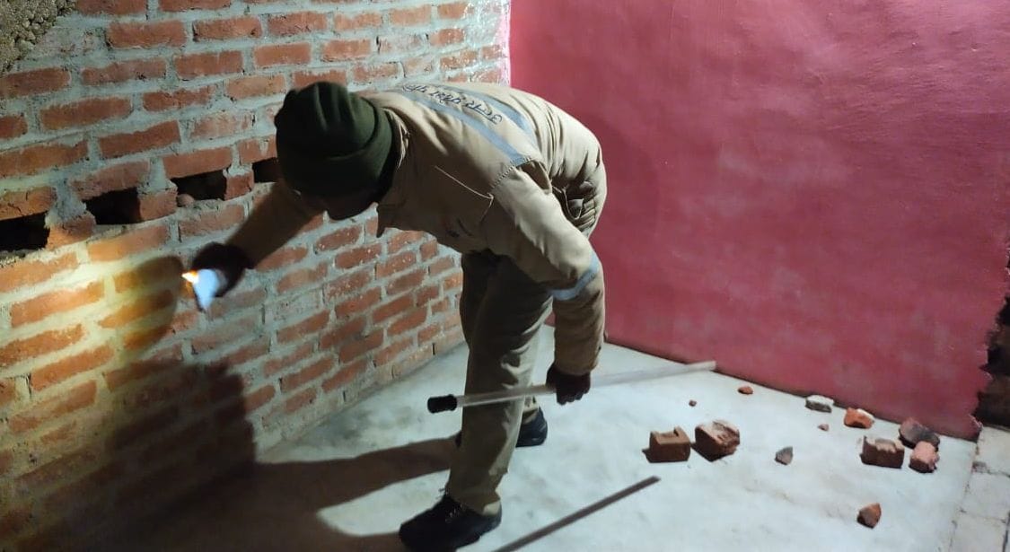 फोटो-35- घर के अंदर पड़े ईंट पत्थरों को देखता पुलिसकर्मी