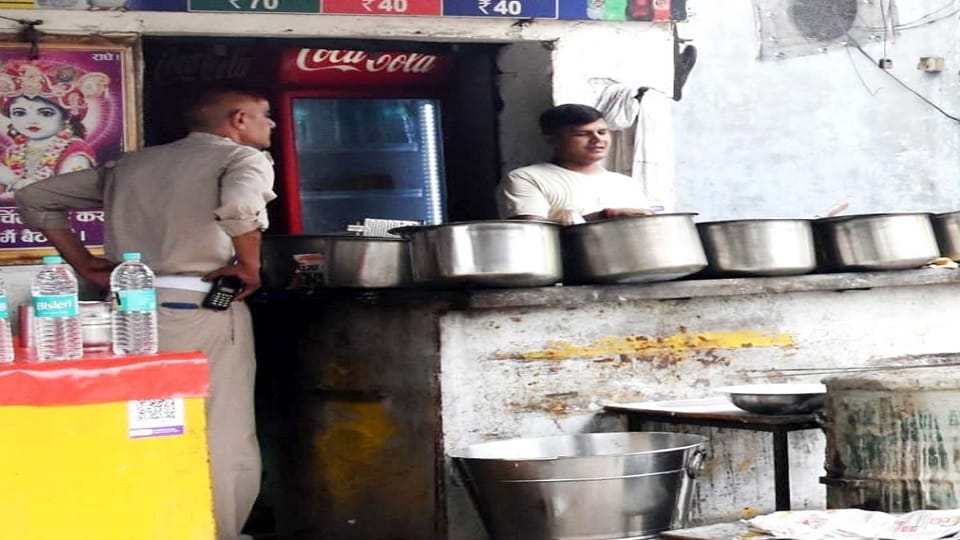 किशनपुर तिराहे पर होटल स्वामी के नाम के पोस्टर के लिए जानकारी देते पुलिसकर्मी