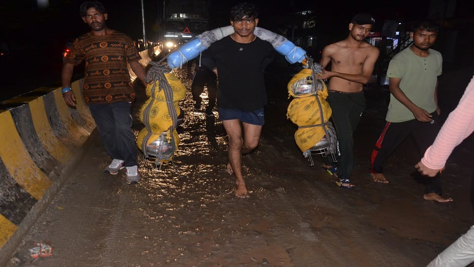 रामघाट रोड पीएसी के पास सड़क पर डाली गई गिट्ट और बालू बारिश के बाद गिट्टियों से नंगे पैर कांवड़ लेकर जाता कांवड़िया