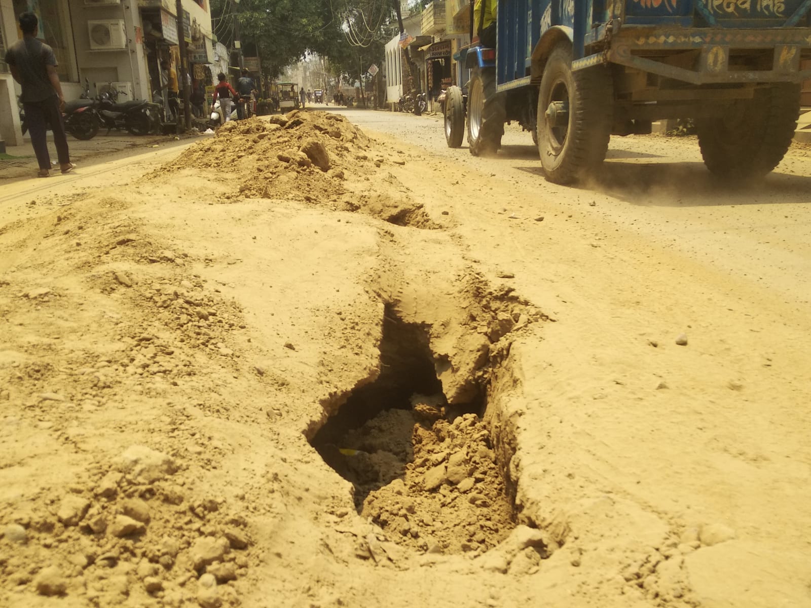 लाल इमली चौराहा पर सड़क की खोदाई के दौरान उड़ती धूल और मुंह ढककर निकलती युवतियां