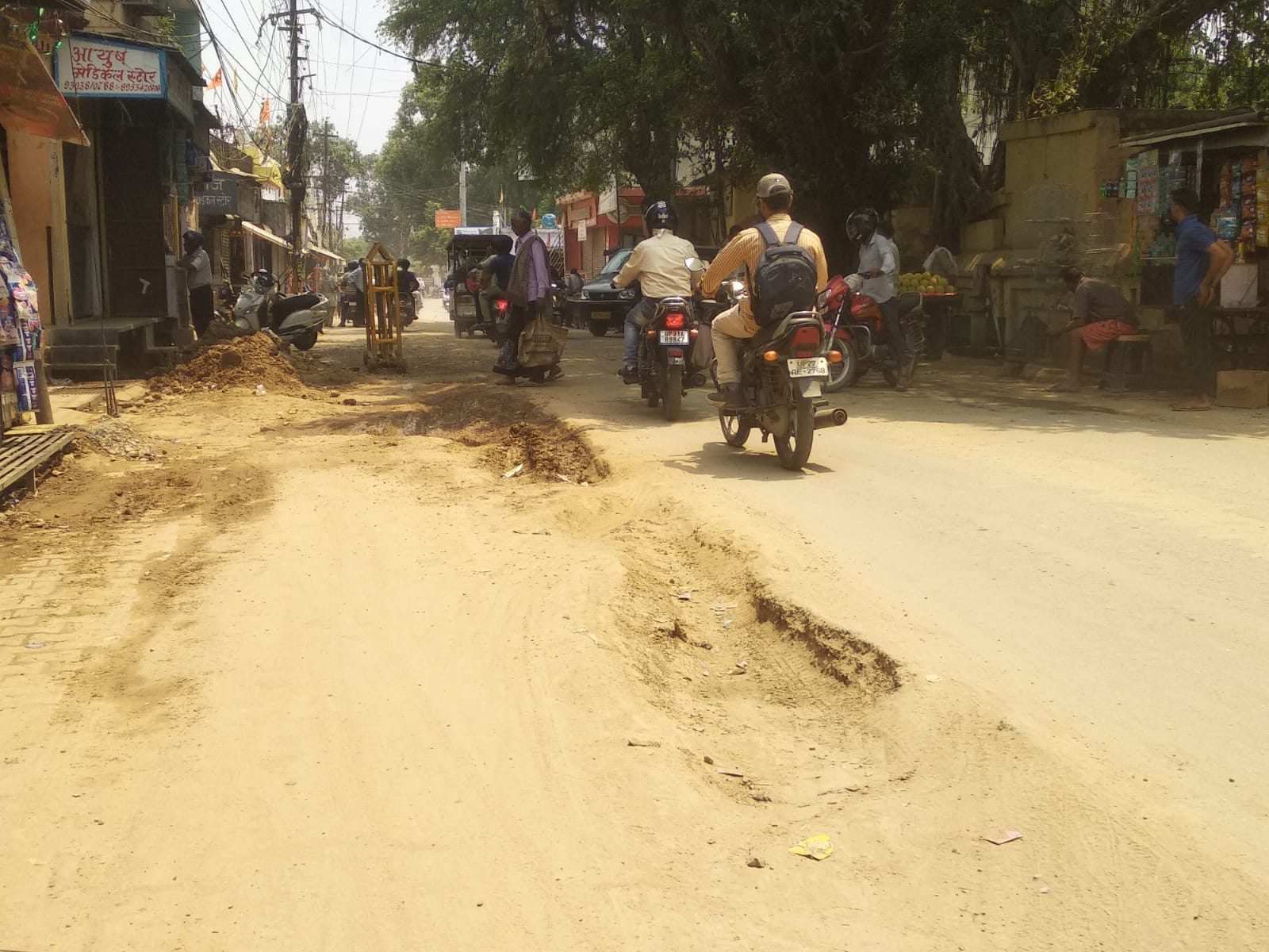 लाल इमली चौराहा पर सड़क की खोदाई के दौरान उड़ती धूल और मुंह ढककर निकलती युवतियां