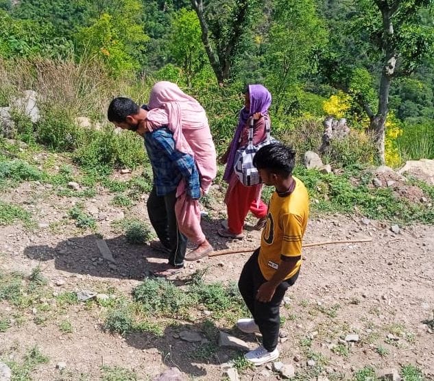 नालागढ़ के रतवाड़ी पंचायत के घाटी गांव में बीमार महिला को पीठ पर उठा कर मुख्य मार्ग तक ले जाता 