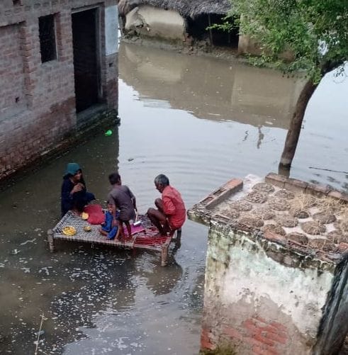 मस्जिद नगला में बाढ़ से जलमग्न एक घर मे चारपाई पर बैठा परिवार। संवाद