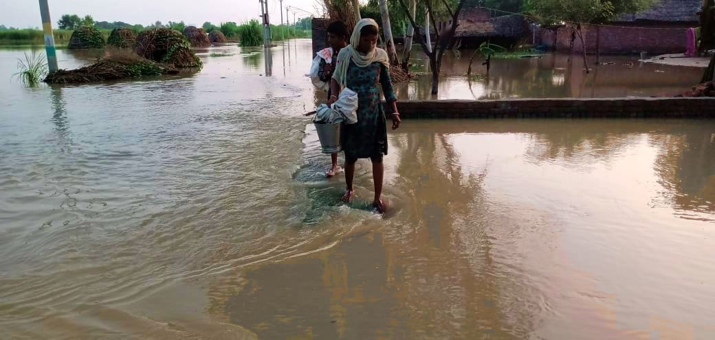मिर्जापुर के जलमग्न ग्राम पैलानी में चारपाई पर भूसा ले जाते युवक। संवाद