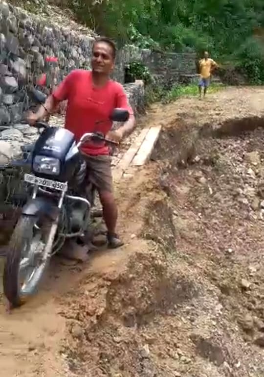 भूस्खलन से बंद बकाहन-केलेवाला सड़क पर बाइक को धक्का मारकर दूसरी तरफ पहुंचाते ग्रामीण। संवाद भूस्खलन से बंद बकाहन-केलेवाला सड़क पर बाइक को धक्का मारकर दूसरी तरफ पहुंचाते ग्रामीण। संवाद